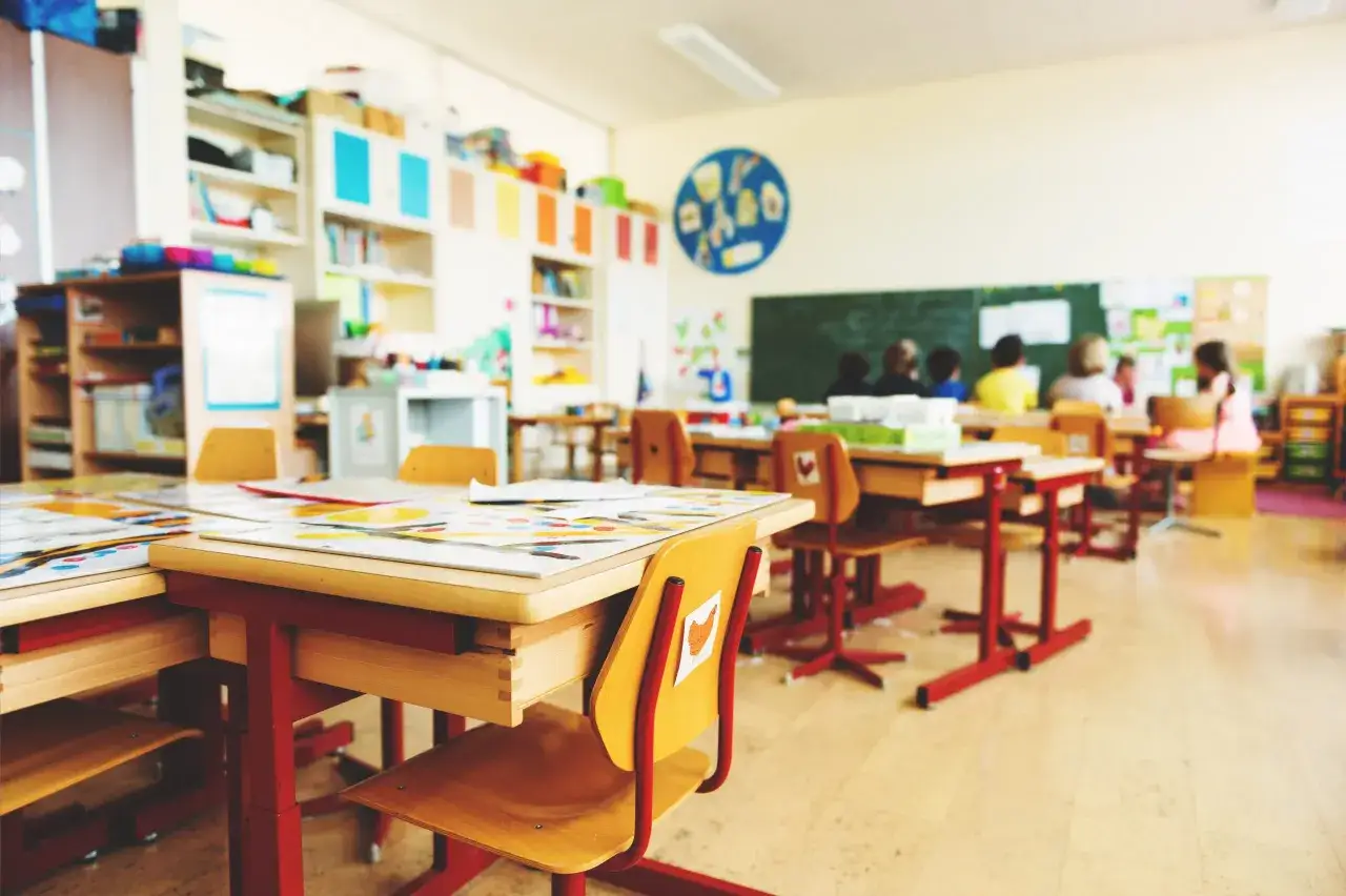 Klassenzimmer mit roten Tischen und St&uuml;hlen. Die Sitzordnung der Grundschule zur Wand ist gut sichtbar, mit Kindern, die an den Tischen sitzen.
