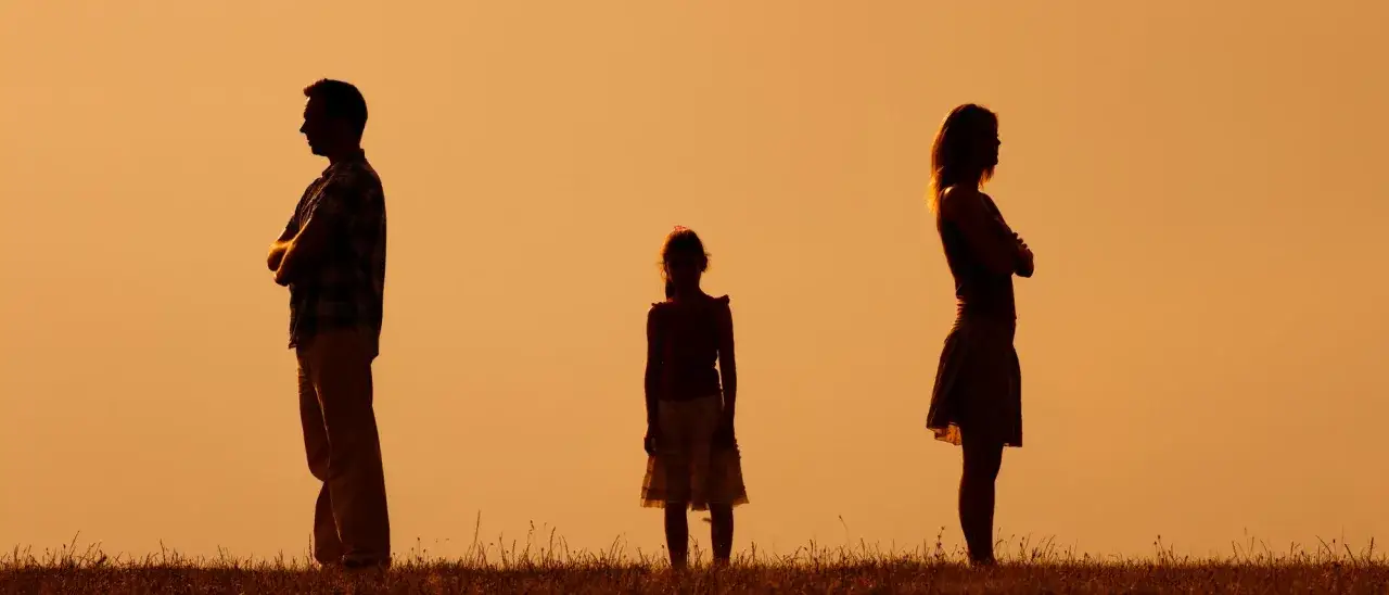 Silhouetten von Eltern, die sich abwenden, w&auml;hrend ein Kind dazwischen steht. Der Trennungsschmerz Kinder ist sp&uuml;rbar.