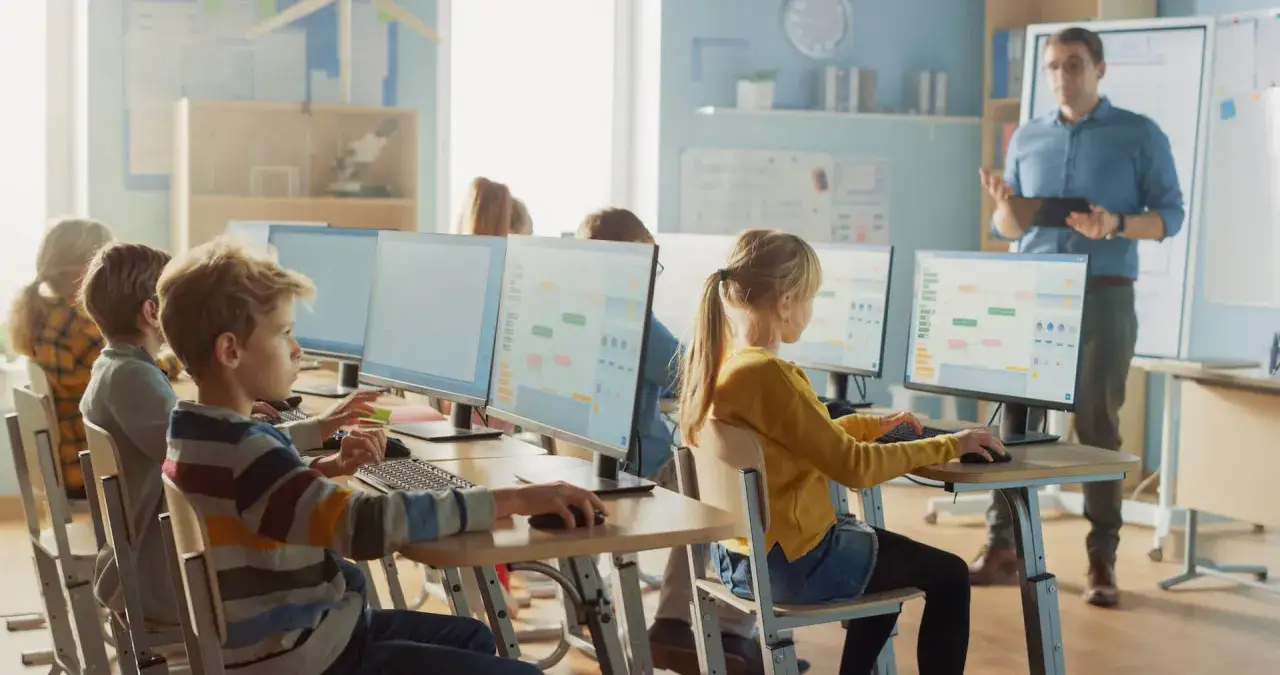 Schüler lernen im digitalen Unterricht an Computern, während der Lehrer Anweisungen gibt.