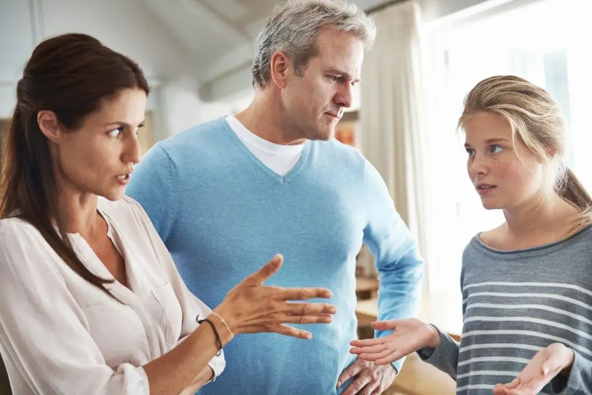 Ein Teenager im Streit mit seinen Eltern. Die Mutter gestikuliert, der Vater schaut streng, die Tochter wirkt ratlos.
