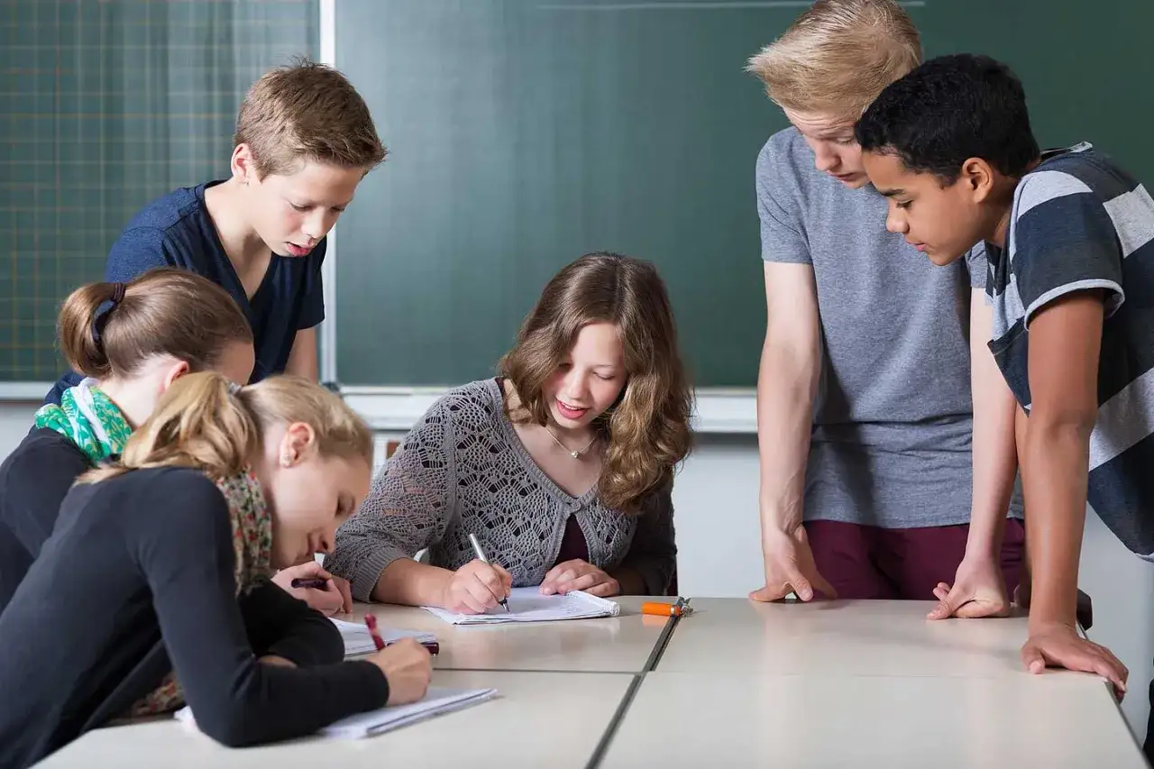 Sechs Sch&uuml;ler, etwa 12 Jahre alt, arbeiten konzentriert an ihren Heften. Ein Junge lehnt sich &uuml;ber den Tisch, um besser zu sehen.