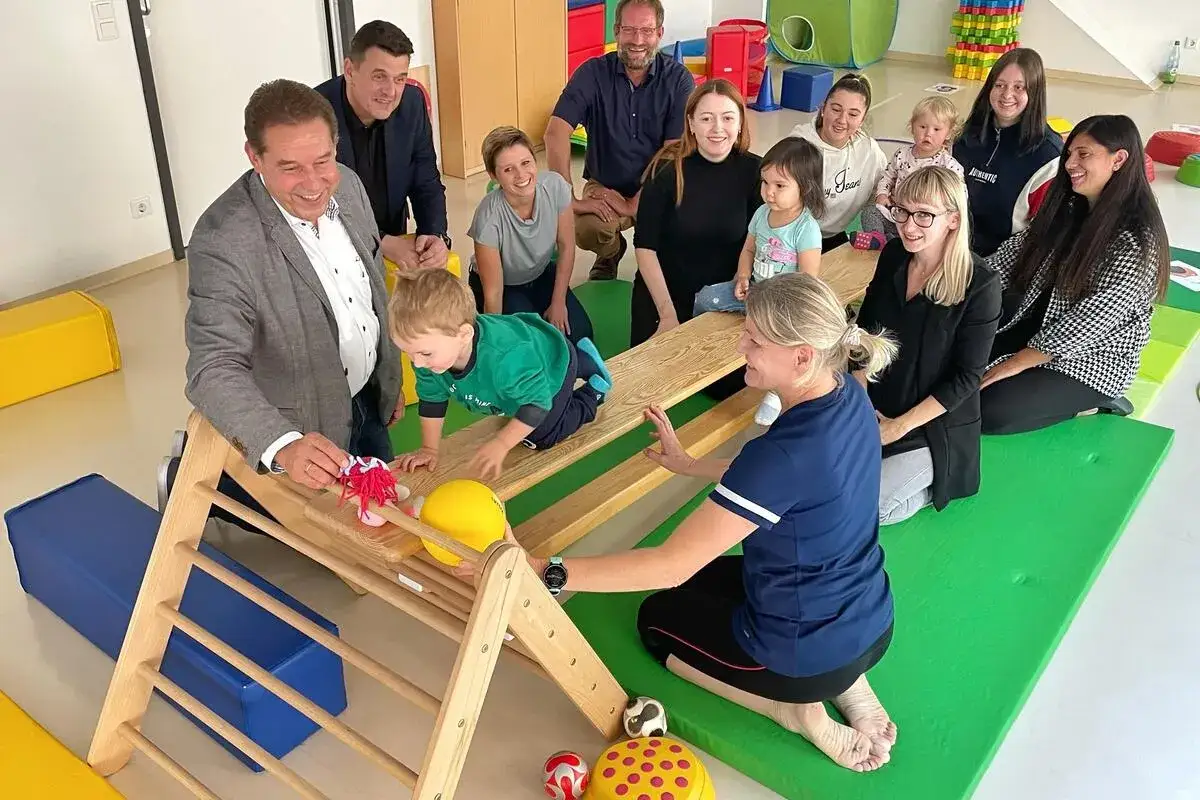 Erwachsene beobachten ein Kind, das auf einem Holzspielgerät klettert. Der Bewegungsdrang von Kindern wird hier gefördert.