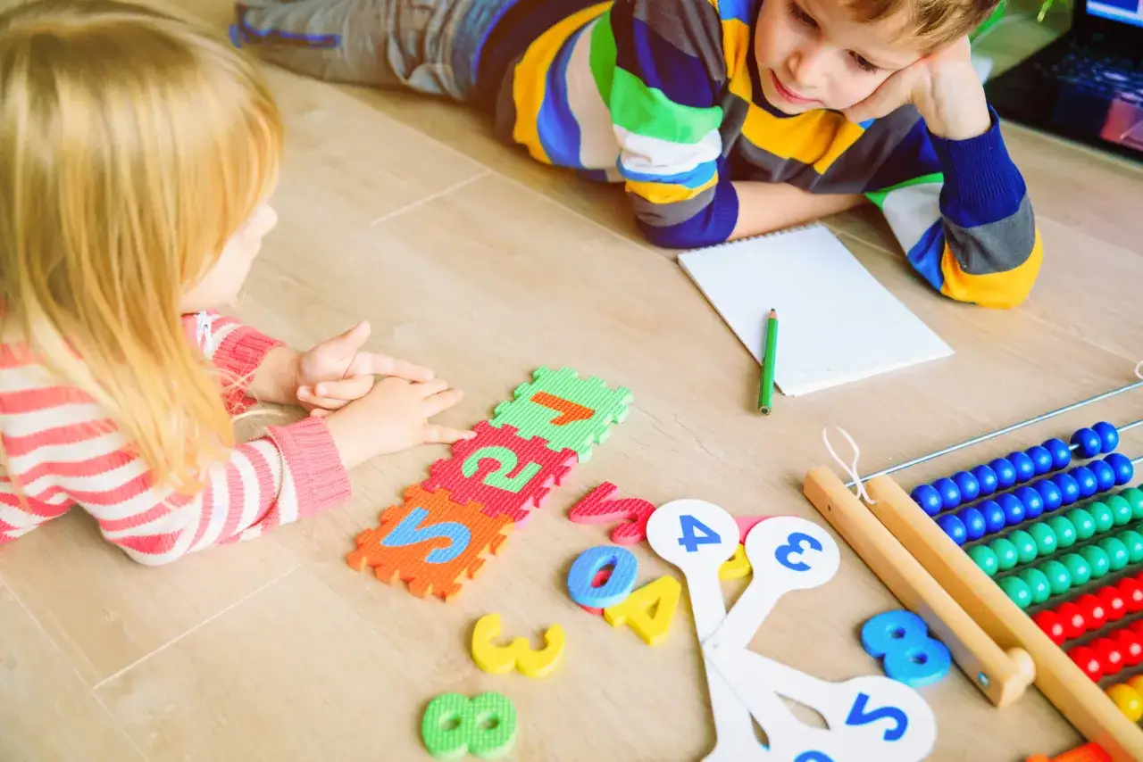 Zwei Kinder lernen spielerisch Mathe mit Zahlenpuzzles, einem Abakus und einem Notizbuch.