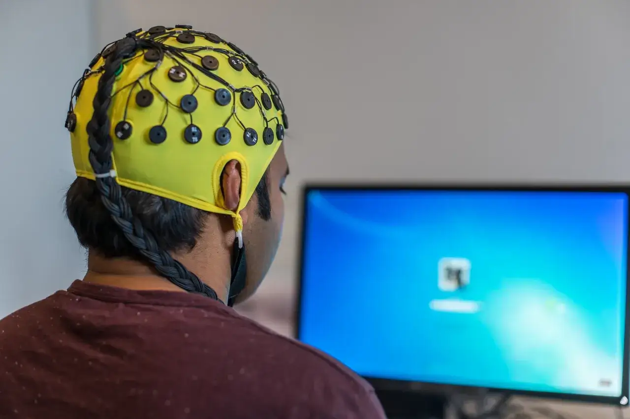 Mann mit EEG-Kappe, die für Biofeedback-Training bei ADHS verwendet wird, blickt auf einen Computerbildschirm.