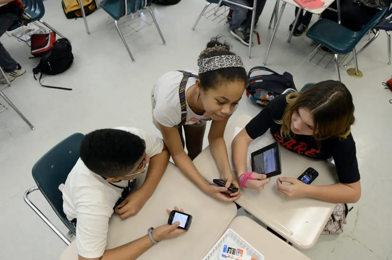 Sch&uuml;ler nutzen digitale Medien im Unterricht: Tablets und Smartphones werden f&uuml;r Lernzwecke eingesetzt, w&auml;hrend sie an ihren Tischen sitzen und zusammenarbeiten.