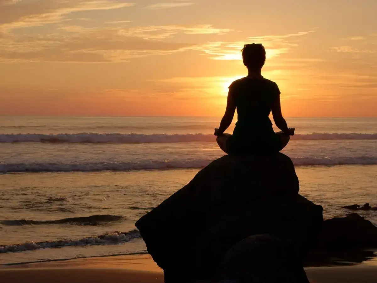 Silhouette einer Person in Meditationshaltung auf einem Felsen am Meer bei Sonnenuntergang. Ein Bild f&uuml;r Selbstregulation Nervensystem.
