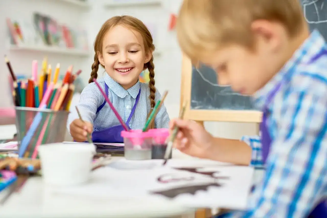 Fröhliche Kinder beim Malen im Förderunterricht Grundschule. Buntstifte und Farben liegen bereit.