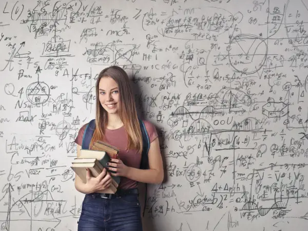 Ein lächelndes Mädchen mit Büchern vor einer Wand voller mathematischer Formeln. Sie zeigt, wie kann man sich in Mathe verbessern: durch Lernen und Üben.